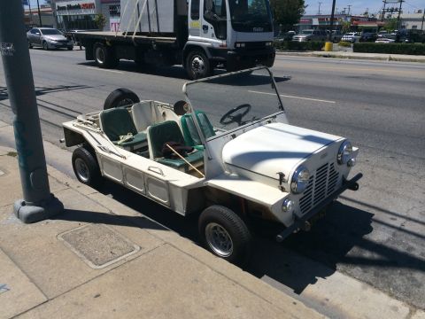 1968 Ford Mustang - A white Mini Moke is parked on the side of a street with a truck driving in the background.