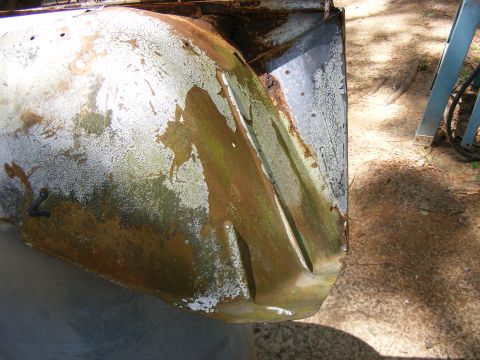 Close-up of a heavily rusted and corroded metal panel, showing peeling white paint and brown/green staining. A