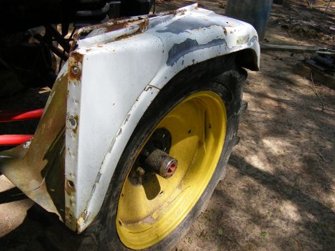 White tractor fender with peeling paint and yellow wheel with knobby tire