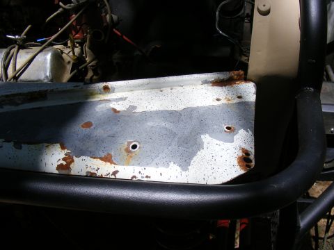 Rusted fender panel with peeling paint and exposed metal, next to black roll bar and engine components