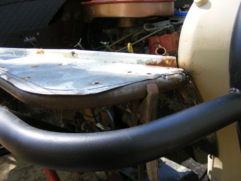 Close-up of a vehicle's engine bay with a black roll bar in the foreground and a tan fender on the right