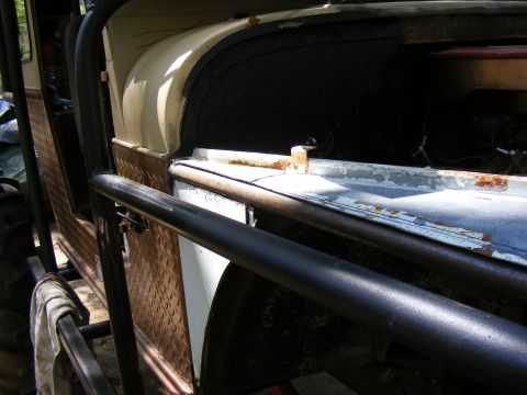 Off-road vehicle side view, showing diamond plate paneling and roll cage. The vehicle is tan and white with ru