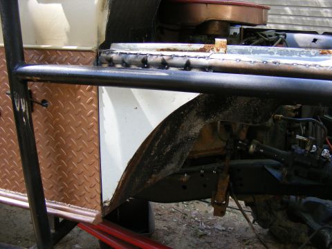 Close-up of a custom roll cage and diamond plate panel on a vehicle's side, showing welded seams and rusty whe
