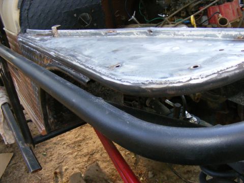 close-up of a vehicle's unfinished metal body panel with a black roll bar in front