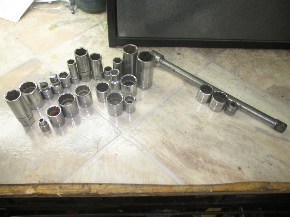 Socket wrench set with various sizes of sockets and a breaker bar on a tiled surface