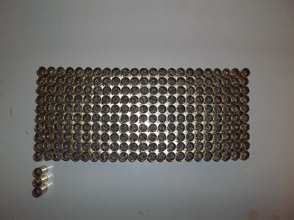 Rectangular arrangement of brass cartridges with dark projectiles, plus three loose cartridges to the left