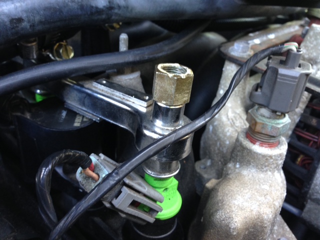 Close-up of a fuel injector with a green plastic tip and a sensor screwed into an engine component
