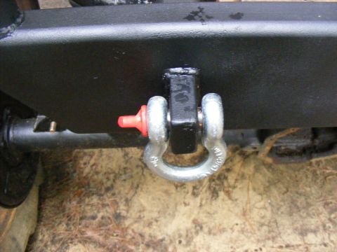 Black tow hitch receiver with a silver shackle attached. Red plastic cap on pin