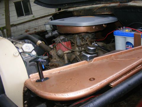 Engine bay with V8 engine, carburetor, and Optima battery. Copper-colored accents on the engine cover and fend