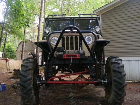 Tan Jeep CJ-5 with large tires and a roll cage, viewed from the front