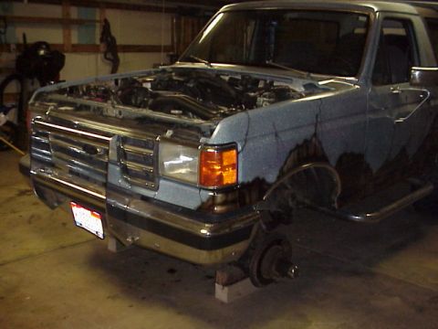 1989 Ford Bronco - This Ford Bronco is in a garage with its front end partially dismantled and wheels removed.