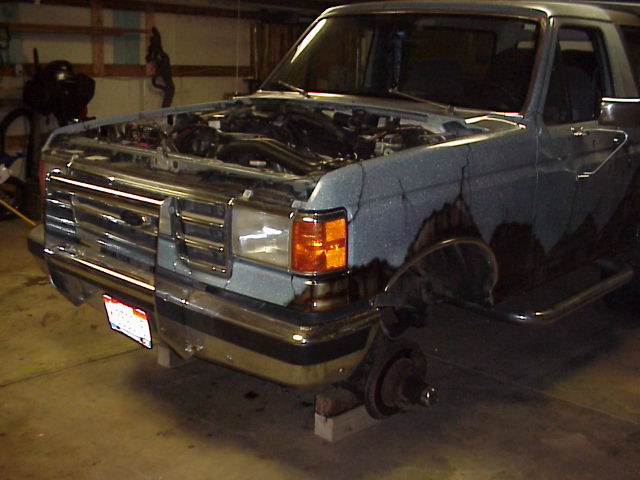 Ford Bronco with hood up, front end disassembled, sitting on blocks in a garage
