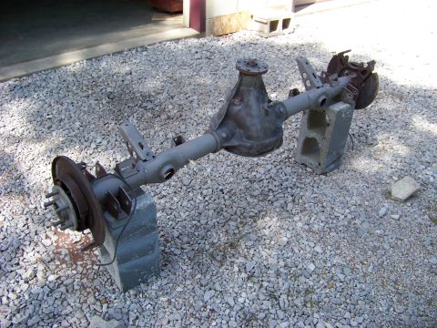 1999 Mercury Grand Marquis - A disassembled rear axle assembly sits on gravel outside a garage.