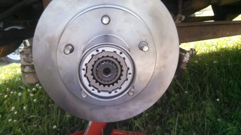 1979 Ford Bronco - Front hub and brake rotor assembly on a vehicle, supported by a jack stand outdoors.