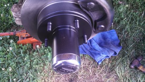 1979 Ford Bronco - Close-up of a vehicle's wheel hub and brake rotor assembly, with a blue cloth and jack visible on the grass.