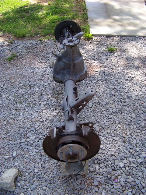 1999 Mercury Grand Marquis - This rear axle assembly, likely from a sedan, is shown disassembled and resting on a gravel surface.