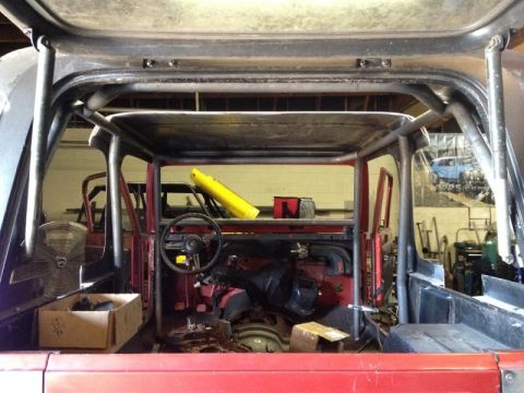 1985 Jeep CJ7 - The interior of a red Jeep is shown, a roll cage and exposed components. Another vehicle is visible in the background.