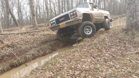 1979 Ford Bronco - A GMC pickup truck is shown off-roading through a muddy, wooded area.