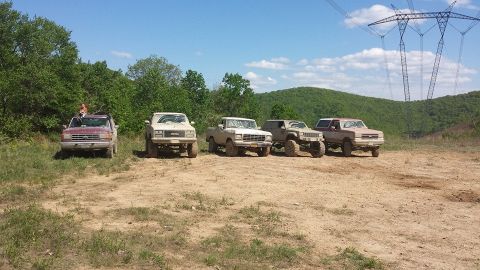 1979 Ford Bronco - A group of off-road vehicles are parked on a dirt trail under a bright blue sky with power lines overhead.