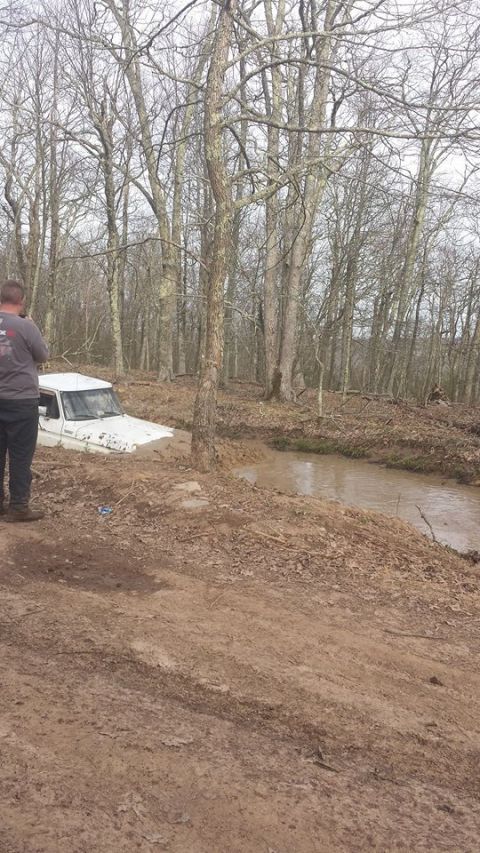 1979 Ford Bronco - A white 1979 Ford Bronco is stuck in a muddy stream surrounded by trees.