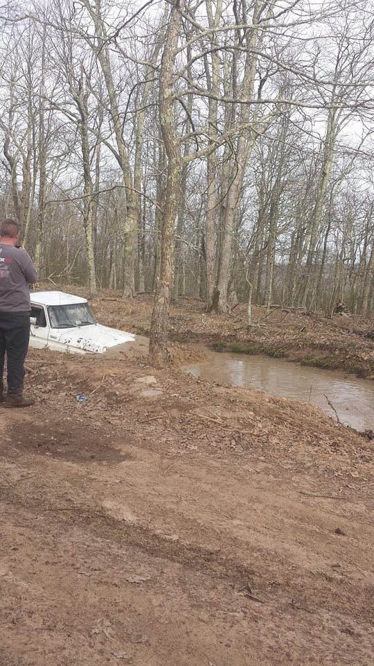 White 1979 Ford Bronco stuck in muddy stream