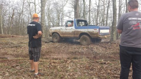 1979 Ford Bronco - A 1979 Ford Bronco navigates a muddy trail in a wooded area.