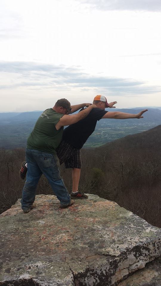 Two guys on a rock overlooking a valley, one doing a dab pose