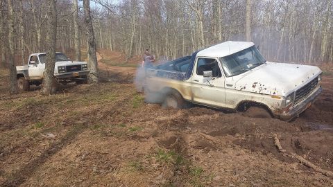 1979 Ford Bronco - Two trucks, a Ford Bronco and a GMC, are stuck in the mud off-road.
