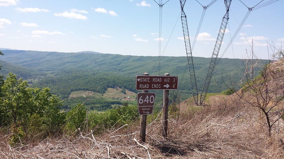View from a hilltop with signs pointing to roads and a valley below. Power lines are visible overhead