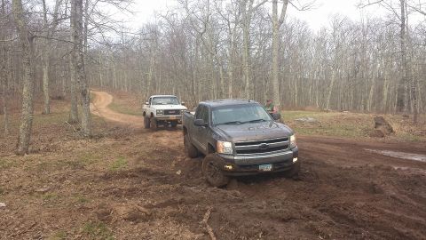 1979 Ford Bronco - Two trucks navigate a muddy, wooded path, with one appearing to be stuck.