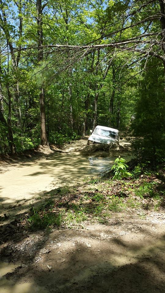 White SUV stuck deep in a muddy trail, surrounded by trees