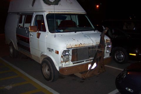 1996 Ford Taurus - A white van, possibly a conversion van, is parked at night with a makeshift bumper attached to its front.
