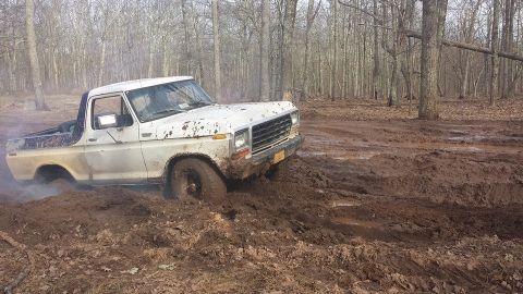 1979 Ford Bronco - A white 1978 Ford Bronco struggles to navigate a muddy forest trail.