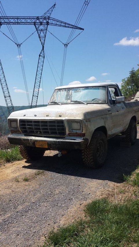 1979 Ford Bronco - A dirty 1979 Ford F-150 pickup truck is parked on a gravel road with power line towers in the background.
