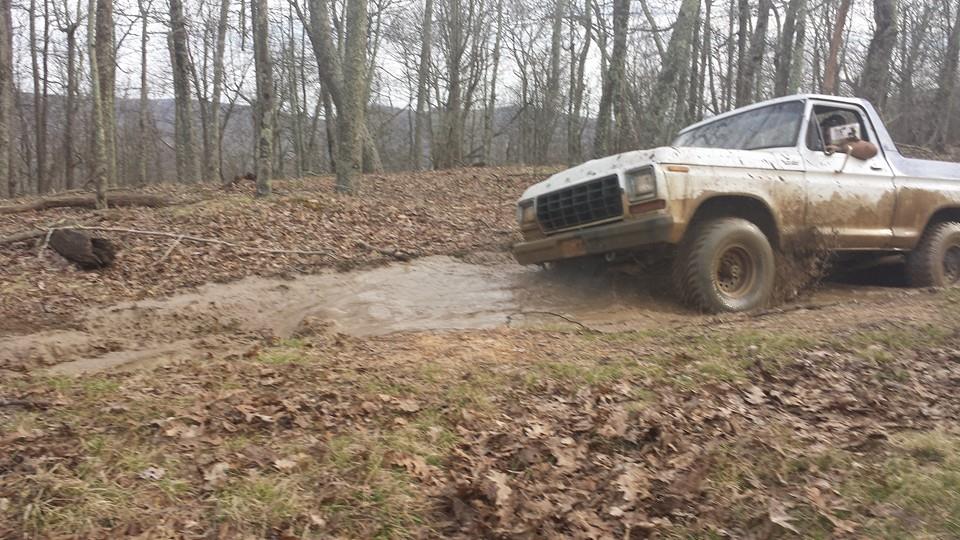 White 1979 Ford Bronco driving through mud in a wooded area
