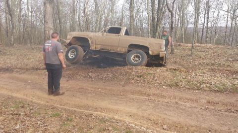 1979 Ford Bronco - A muddy pickup truck is stuck on a hill with two men observing the situation.