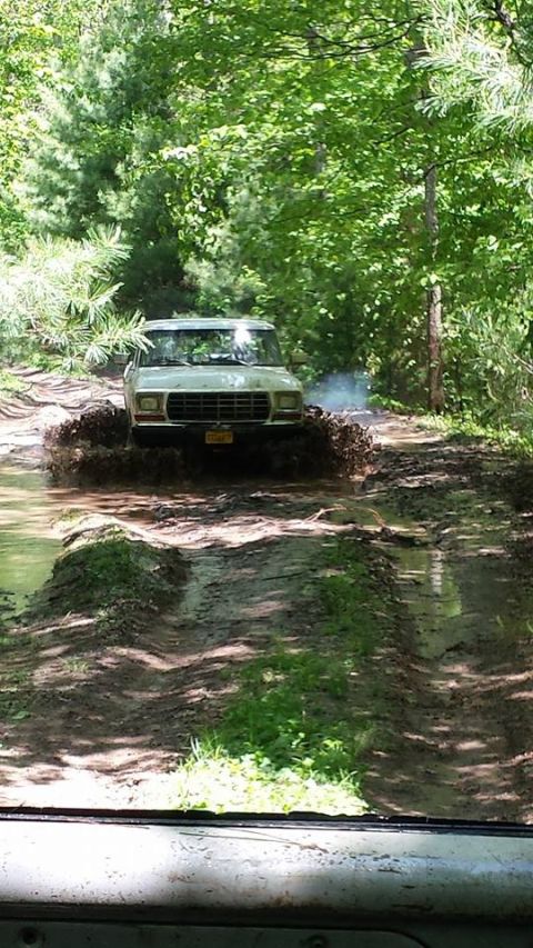 1979 Ford Bronco - A white 1978 Ford Bronco navigates a challenging muddy path in a wooded area.