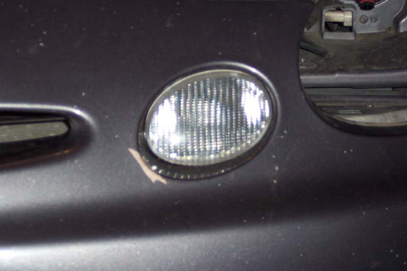 Dark gray car bumper with a chipped fog light assembly and a visible Supermotors.net logo