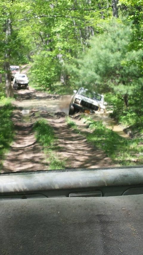 1979 Ford Bronco - Multiple off-road vehicles navigate a challenging muddy path through a dense forest.