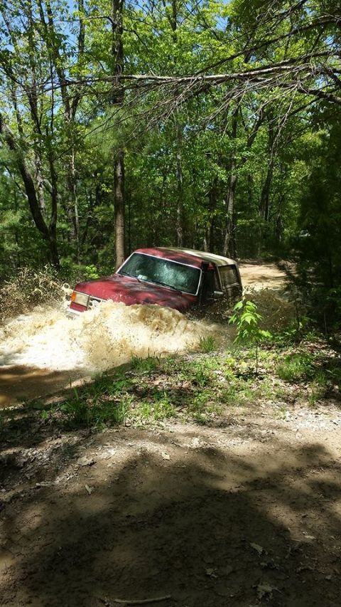1979 Ford Bronco - A red 1979 Ford Bronco navigates a water obstacle on a wooded trail.
