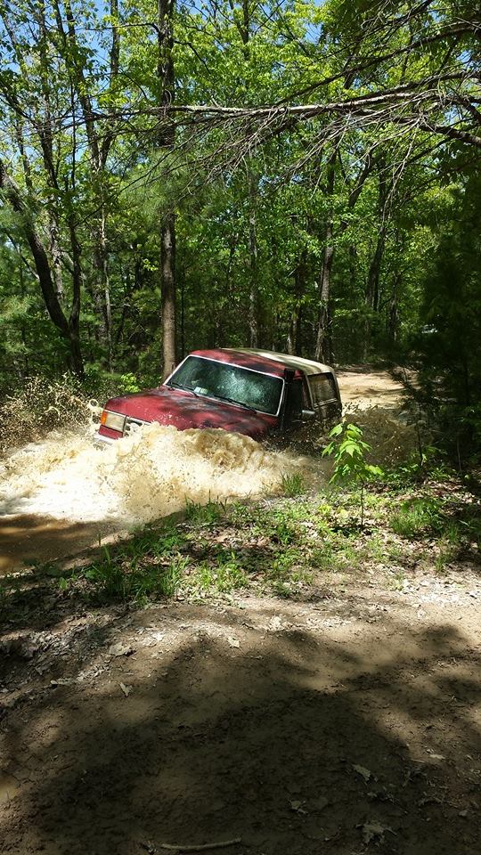 Red 1979 Ford Bronco splashing through a muddy trail