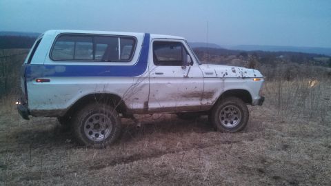 1979 Ford Bronco - A white and blue Ford Bronco is seen from the side, covered in mud, in an outdoor setting.