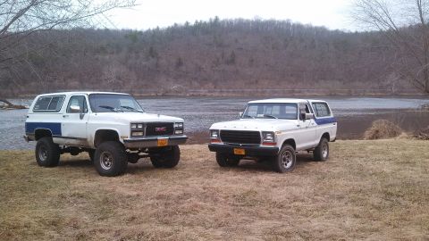 1979 Ford Bronco - Two SUVs, a Ford Bronco and a GMC Jimmy, are parked side-by-side near a body of water.