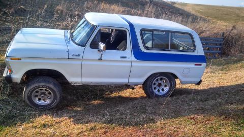 1979 Ford Bronco - White and blue Ford Bronco with off-road tires parked on a grassy hill.