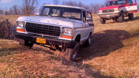 1979 Ford Bronco - Two Ford Broncos are parked on a dry, grassy hill under a partly cloudy sky.