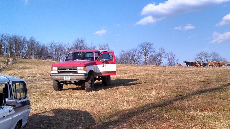 Red and white pickup truck, 1987 model year, parked on a grassy hill with an open door