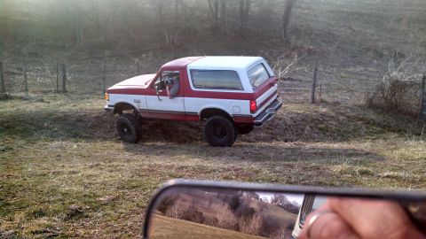 1979 Ford Bronco - Ford Bronco with a lifted suspension is driven off-road through a grassy field.
