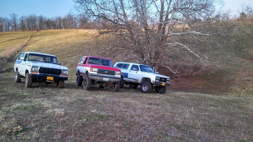White 1979 Ford Bronco, red and white SUV, and white GMC SUV parked on a hill