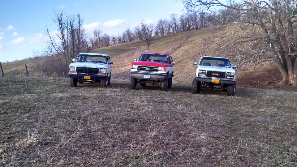 Three pickup trucks parked on a grassy hill