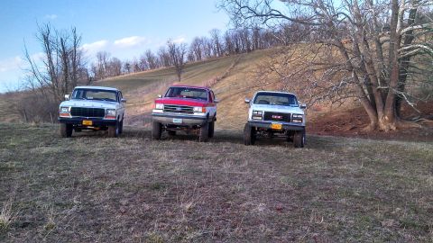 1979 Ford Bronco - Three pickup trucks are parked on a grassy hill under a clear sky.